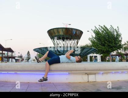 guy se trouve sur le bord de la fontaine dans le place de la ville Banque D'Images