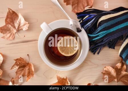 Concept automnal avec détail d'une tasse avec thé rouge et citron sur une écharpe sur une table en bois avec des feuilles sèches sur le dessus. Vue de dessus Banque D'Images