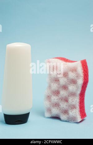 Flacon de cosmétiques blanc et bain poreux rouge et blanc eponge sur le côté contre le fond de papier bleu avec une mise au point sélective Banque D'Images