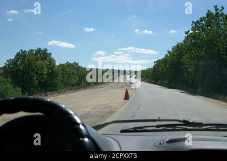 Volant flou d'une voiture roulant à moitié réparé route de campagne avec ciel bleu et nuages blancs Banque D'Images