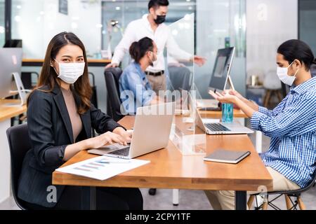 Portrait d'un employé de bureau asiatique femme d'affaires porter un masque de protection travailler dans un nouveau bureau normal avec une équipe interraciale en arrière-plan en tant que social dist Banque D'Images