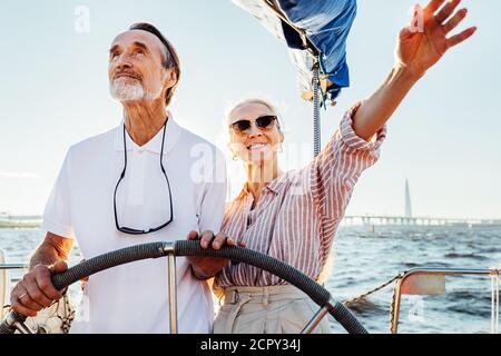 Couple mature debout au volant sur leur yacht et vacances agréables Banque D'Images