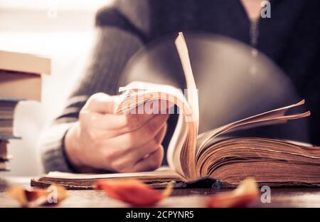 Homme défilant rapidement de vieilles pages de livre à la table en bois Banque D'Images