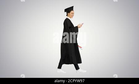 Femme souriante diplômée en mortaboard textant sur son téléphone Banque D'Images