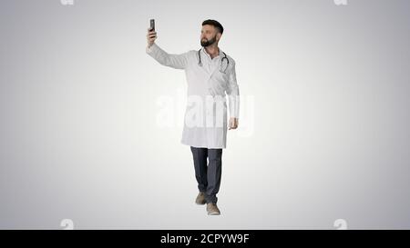 Médecin prenant un selfie avec un smartphone tout en marchant sur un gradient Banque D'Images
