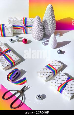 Cadeaux de Noël avec ruban arc-en-ciel aux couleurs du drapeau de la communauté LGBTQ. Décorations de Noël, boules disco, sapin en céramique, papier arc-en-ciel, ruban et Banque D'Images