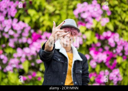 Joyeux gai beau branché alternative jeune homme adolescent portrait souriant sur l'appareil photo avec arrière-plan coloré de parc de fleurs - diversité et Banque D'Images