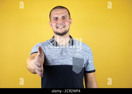 Homme russe debout sur fond jaune insolé offrant souriant et amical se faire une poignée de main comme un accueil et un accueil chaleureux Banque D'Images