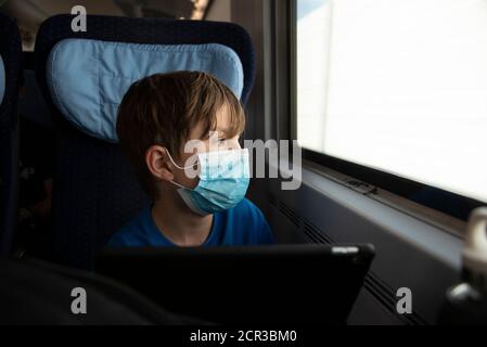 Le garçon est assis dans un train portant un masque, un respirateur, un masque médical, une protection de la bouche et du nez Banque D'Images