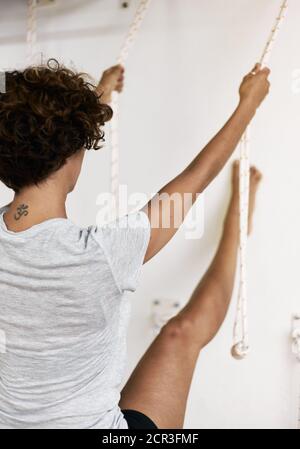 Jeune femme pratiquant le yoga iyengar en utilisant des cordes murales en studio, supta padangusthasana Banque D'Images