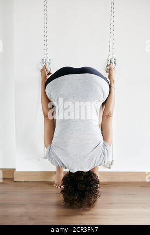 Jeune femme pratiquant le yoga iyengar en utilisant des cordes murales en studio, supta padangusthasana Banque D'Images