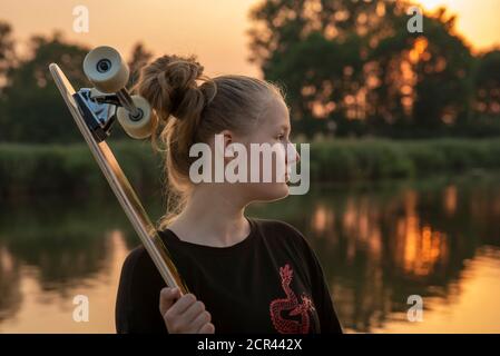 Une fille se tient au bord du lac avec une longue barde au coucher du soleil Banque D'Images