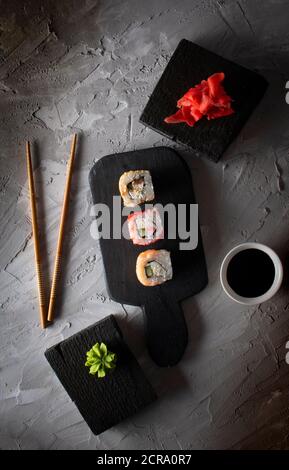 Repas japonais sur fond sombre. Trois petits pains à sushis sur une planche de cuisine noire. Cuisine asiatique avec baguettes Banque D'Images