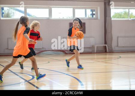 Enfants dans des vêtements de sport brillants jouant au basket-ball ensemble et à la course à pied Banque D'Images