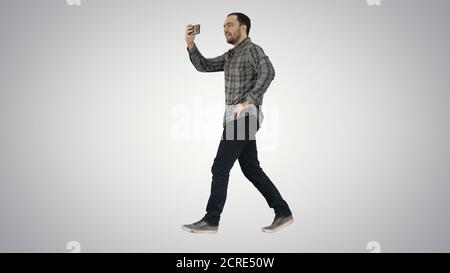 Jeune homme prenant des photos avec un smartphone tout en marchant sur un gradient Banque D'Images