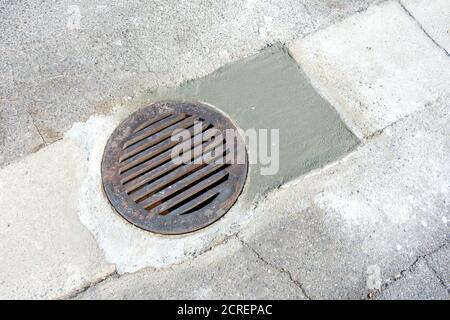 Grille ronde d'évacuation d'orage sur le trou d'homme juste réparé sur la route. Banque D'Images