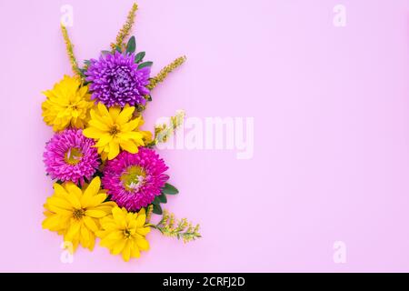 Bouquet d'asters violets et pâquerettes jaunes sur fond de papier rose, maquette avec espace de copie pour le texte. Modèle de fête, motif floral. Carte cadeau avec Banque D'Images