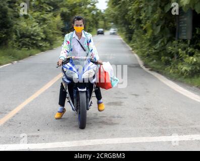 NAKHON NAYOK, THAÏLANDE, JUL 04 2020, UNE jeune femme avec une fronde de visages debout avec une moto à une intersection et attend un tour. Banque D'Images