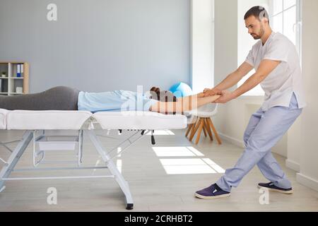 Homme chiropraticien ou ostéopathe étirant la femme patients bras et dos pendant la visite dans la clinique de thérapie manuelle Banque D'Images