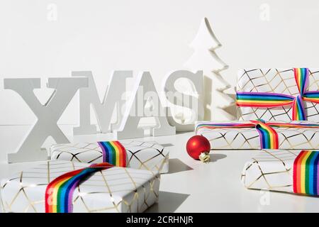 Cadeaux de Noël avec ruban arc-en-ciel aux couleurs du drapeau de la communauté LGBTQ. Décorations de Noël, boules, sapins en céramique et boîtes-cadeaux emballées. Banque D'Images