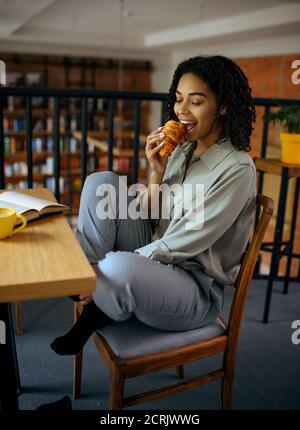 Une jolie étudiante mange des croissants au café Banque D'Images