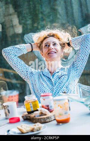 Blonde jeune femme mature en pyjama à la maison à l'heure du petit déjeuner, auto-absorbé. Banque D'Images