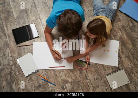 Vue de dessus du petit garçon caucasien et de la fille couché le parquet à la maison et dessin sur un blanc feuille de papier avec crayons colorés Banque D'Images