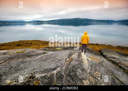 Vue panoramique sur le fjord. Le jeune homme debout sur la roche et regardant la mer. Magnifique paysage de montagne au coucher du soleil. Nature scandinave. N Banque D'Images