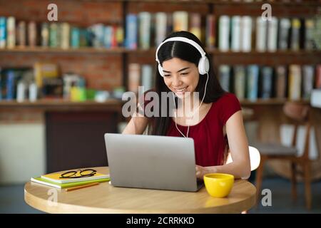 Formation en ligne. Une femme coréenne joyeuse étudiant avec un ordinateur portable et un casque au café Banque D'Images