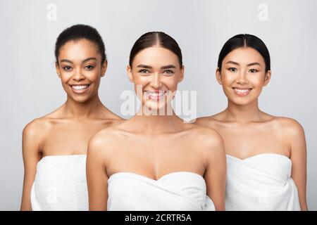 Trois femmes heureuses enveloppées de serviettes sur fond gris Banque D'Images