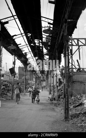 Les gens qui marchent dans les ruines brûlées du centre-ville à la suite des dégâts causés par le grand tremblement de terre Hanshin de 1995 à Kobe, au Japon. Un homme peut être vu dans la distance arrêté et prier. Banque D'Images