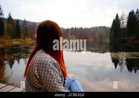 fille de cheveux rouges debout près du lac pendant la saison d'automne avec réflexion du feuillage et de l'eau Banque D'Images