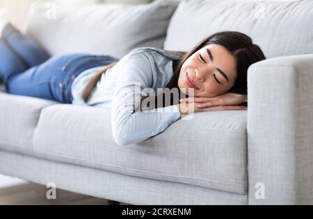 Journée de repos à la maison. Femme asiatique décontractée qui s'est couchée sur un confortable canapé Banque D'Images