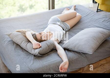 Femme millénaire souriante couchée au lit à la maison, appréciant son temps de week-end paresseux Banque D'Images