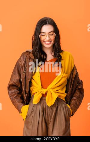 jeune femme en tenue d'automne debout avec les mains dans les poches et en regardant vers le bas isolé sur orange Banque D'Images