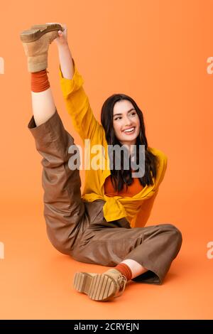 femme tendance en tenue d'automne s'étirant sur les jambes et s'asseyant sur orange Banque D'Images