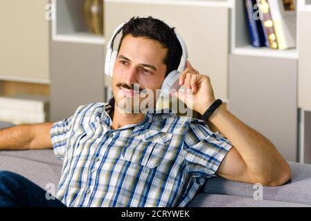 Homme se détendant en écoutant de la musique sur un casque stéréo canapé confortable à la maison souriant avec plaisir dans un concept de divertissement personnel Banque D'Images