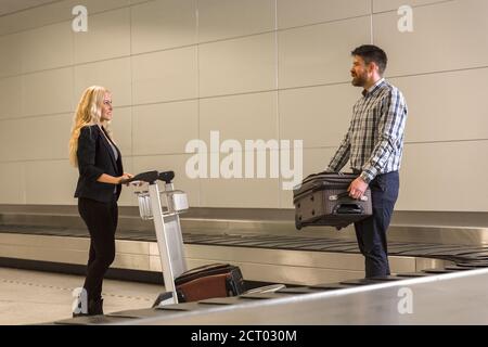 Homme et femme adultes mettant des valises du carrousel à bagages à chariot à l'aéroport Banque D'Images