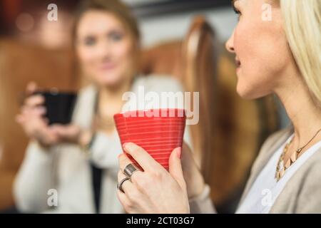 Crochez une femme adulte qui boit une boisson chaude près d'un ami flou cafétéria Banque D'Images