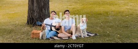 récolte panoramique de l'adolescent et de son père assis sur une couverture presque golden retriever sous le tronc de l'arbre Banque D'Images