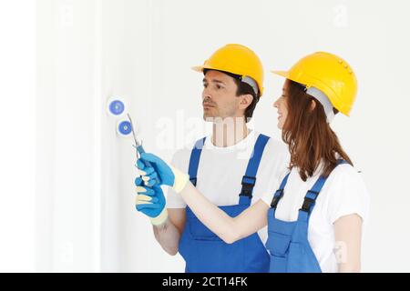 Deux jeunes travailleurs en uniforme de peinture de combinaison et de casque mur blanc Banque D'Images