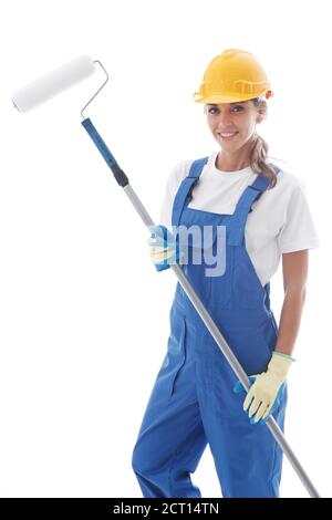 Femme peintre de maison en combinaison uniforme bleue et chapeau rigide jaune avec rouleau à peinture isolé sur fond blanc Banque D'Images