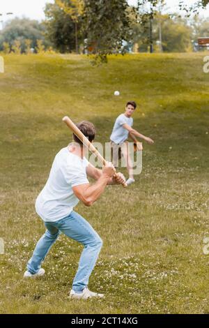 vue arrière du père tenant une batte de softball pendant qu'il joue au baseball avec un adolescent Banque D'Images