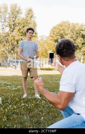 mise au point sélective d'un fils adolescent posé pendant que le père prend des photos sur le smartphone en position de stationnement Banque D'Images