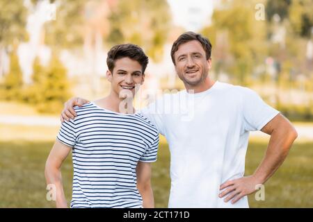 homme debout avec la main sur la hanche et embrassant le fils adolescent extérieur Banque D'Images