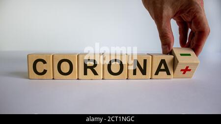 Symbole d'un test de corona négatif. La main masculine tourne un cube et change l'expression 'corona plus' en 'corona moins'. Magnifique fond blanc. Busi Banque D'Images