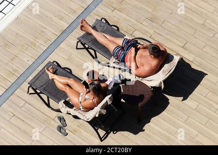 Couple allongé dans des chaises longues et bains de soleil près de la piscine, vue de dessus. Femme en maillot de bain et homme en malles utilisant un smartphone sur une plage Banque D'Images