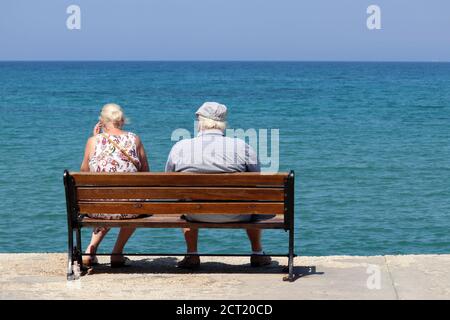 Femme et homme âgés assis sur un banc en bois sur fond bleu de mer, vue arrière. Vieux couple sur une plage, se détendre et profiter de la vie en retraite Banque D'Images