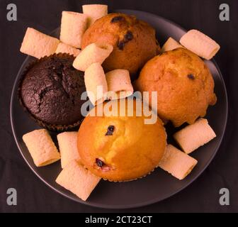 Cupcakes et pop-corn dans une assiette noire sur un noir arrière-plan Banque D'Images