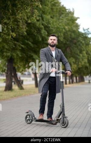 Jeune homme d'affaires élégant debout sur un scooter électrique en milieu urbain Banque D'Images